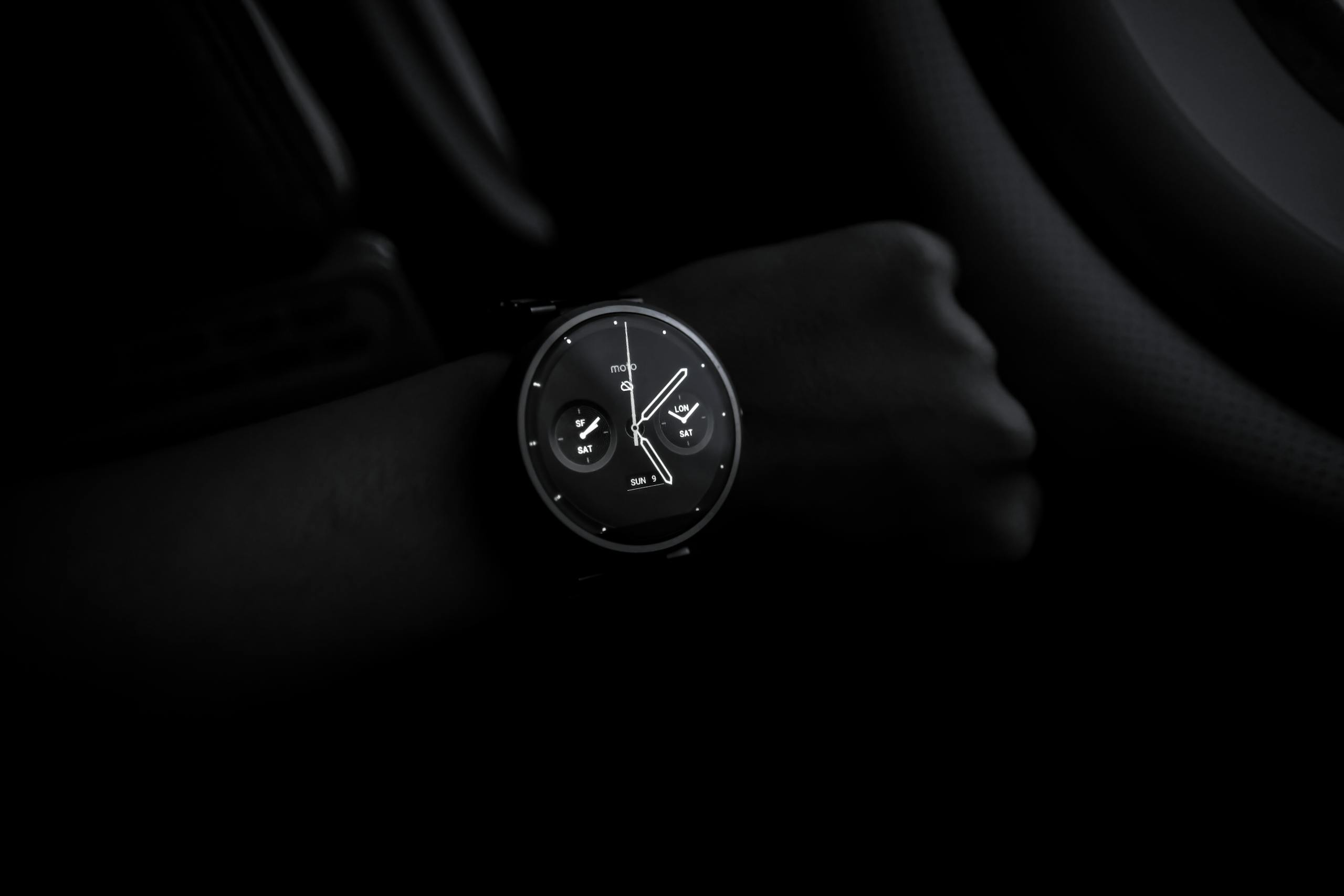 A sleek Moto 360 smartwatch showing time on a wrist in a dimly lit setting, emphasizing its modern design and technology.